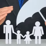 Une personne en costume tient un parapluie en papier au-dessus des silhouettes découpées d'une famille - deux adultes et deux enfants - symbolisant la protection et la sécurité.