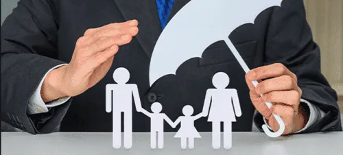 Une personne en costume tient un parapluie en papier au-dessus des silhouettes découpées d'une famille - deux adultes et deux enfants - symbolisant la protection et la sécurité.