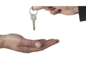 Une main qui passe une clé sur un trousseau à une autre main ouverte en dessous, symbolisant l'acte de donner ou de recevoir des clés, comme lors de la location, de l'achat ou du transfert d'une propriété.