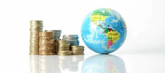 Des piles de pièces de monnaie assorties sont disposées à côté d'un petit globe sur une surface blanche réfléchissante, symbolisant la finance et l'économie mondiales.