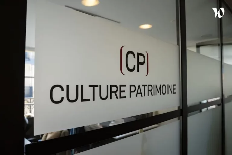 Une porte de bureau en verre sur laquelle sont imprimés en lettres noires les mots (CP) CULTURE PATRIMOINE, avec des panneaux en verre dépoli et des reflets de lumière en arrière-plan.