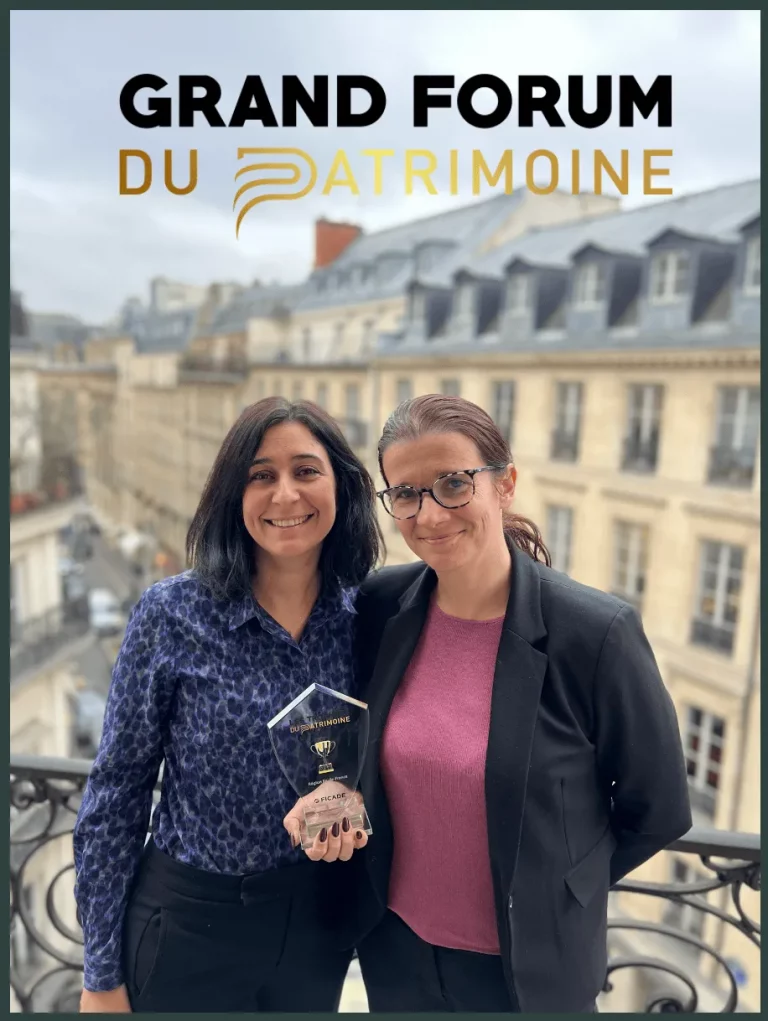 Deux femmes se tiennent sur un balcon en tenant un trophée et en souriant à l'appareil photo. Une rue de la ville et des bâtiments classiques sont à l'arrière-plan. Au-dessus d'elles se trouve le texte GRAND FORUM DU PATRIMOINE.