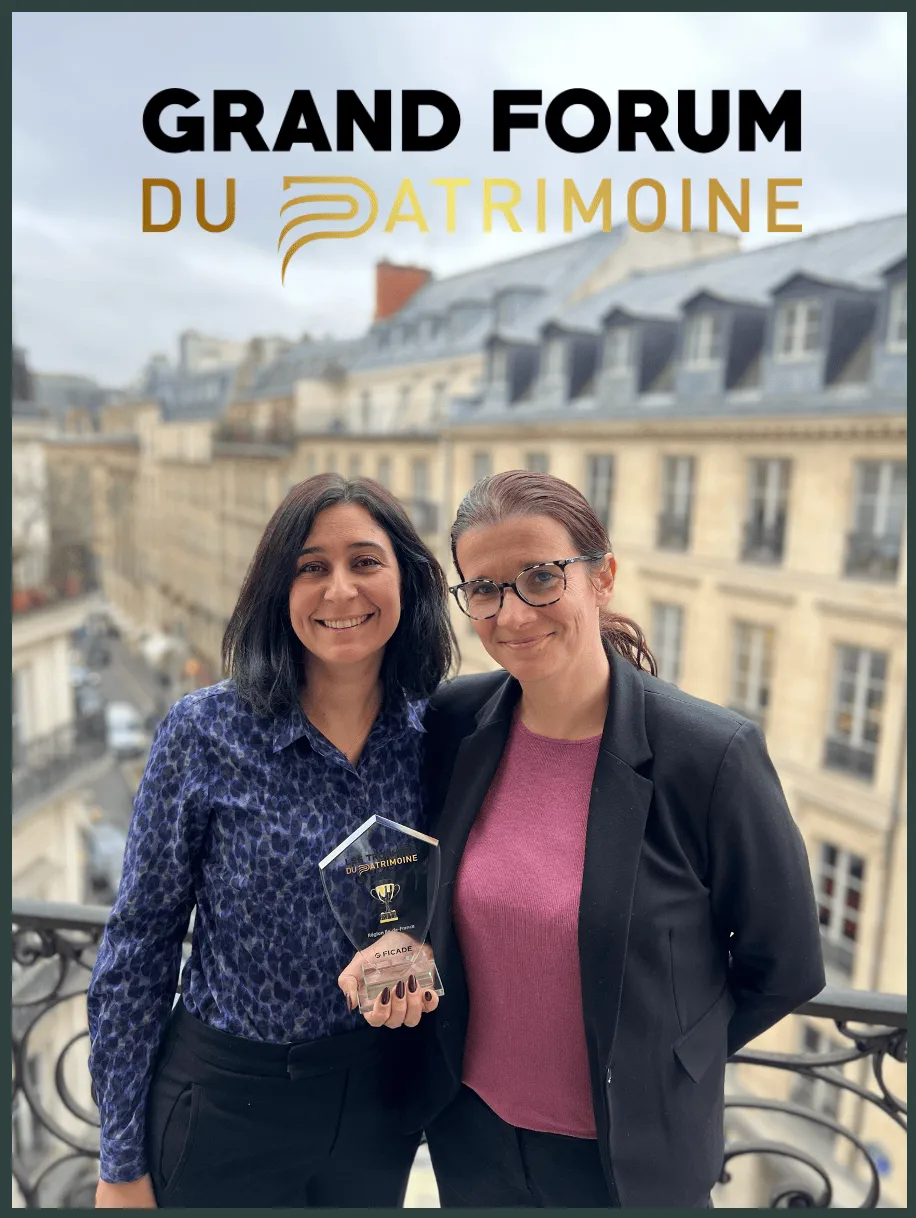 Deux femmes se tiennent sur un balcon en tenant un trophée et en souriant à l'appareil photo. Une rue de la ville et des bâtiments classiques sont à l'arrière-plan. Au-dessus d'elles se trouve le texte GRAND FORUM DU PATRIMOINE.